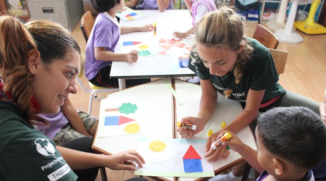 Two Projects Abroad volunteers help a small group of children with a colouring activitty at a daycare centre in Thailand. Projects Abroad Childcare volunteers work with children at a daycare centre in Thailand to complete a colouring activity.